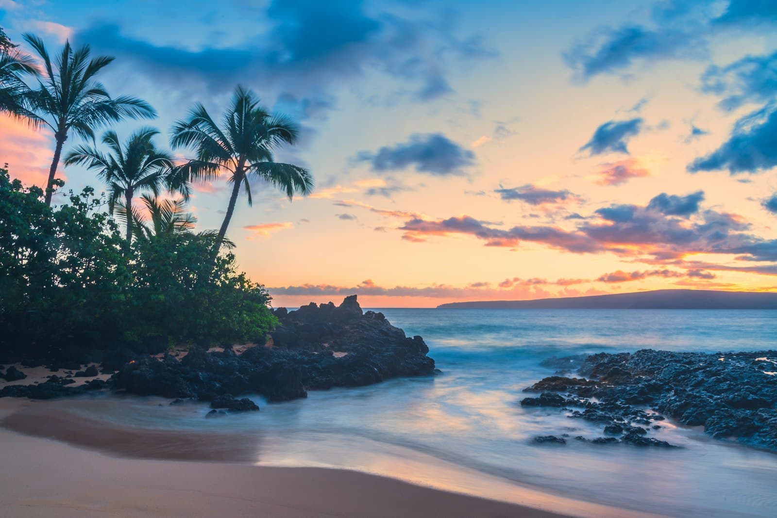 Palm trees and lava rocks over a secluded Maui beach at sunset