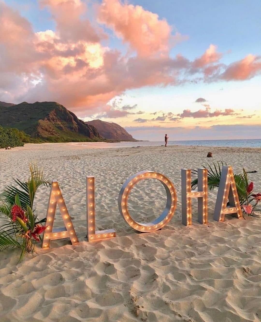 Lighted ALOHA sign on a west Oahu beach with mountains at sunset